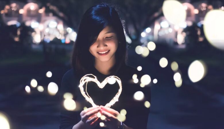 Woman in darkness holding a lit up heart signifying dating herself