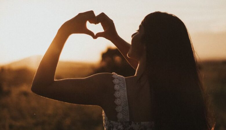 single woman in field making heart with her hands signifying self love