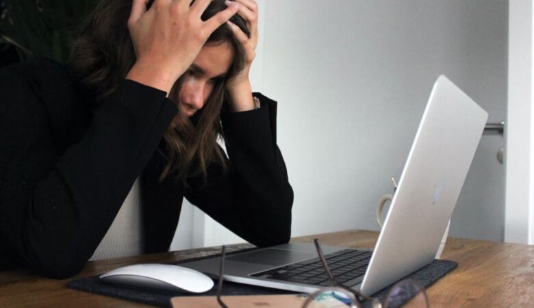 woman with head in hands in front of laptop as she's struggling at university