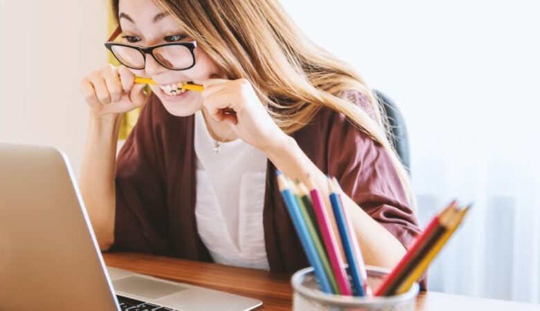 Woman at work staring at laptop and stressfully biting on pen