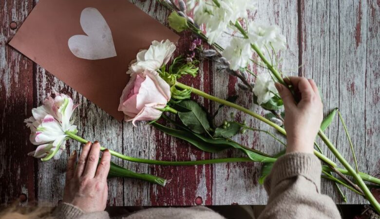 Woman's hands Arranging pink flowers and white heart card for Valentine's Day