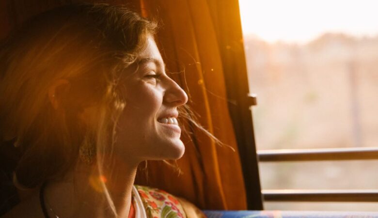 smiling single woman peering out of train window at sunset