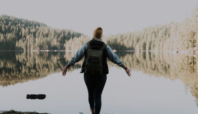 woman stood by lake arms outstretched celebrating single