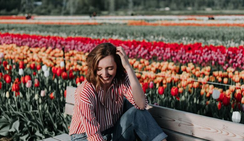 Happy single woman on a bench in a field with multi-coloured flowers in backdrop