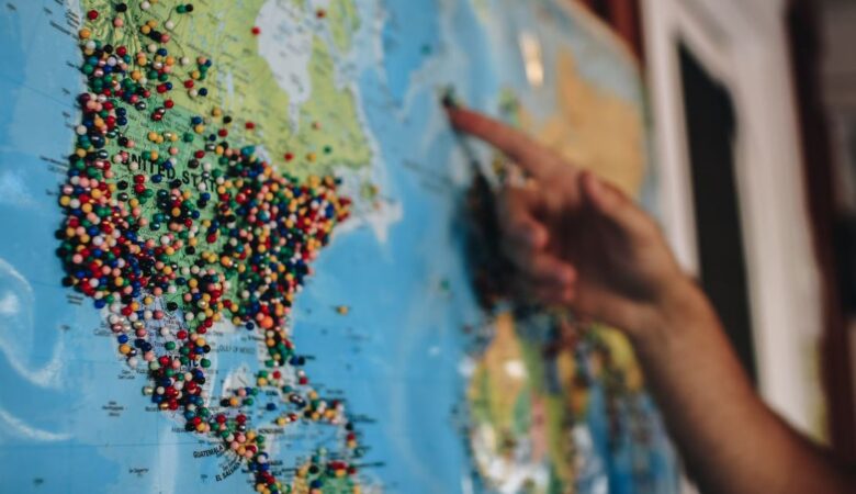 a hand pointing at a pin infested world map