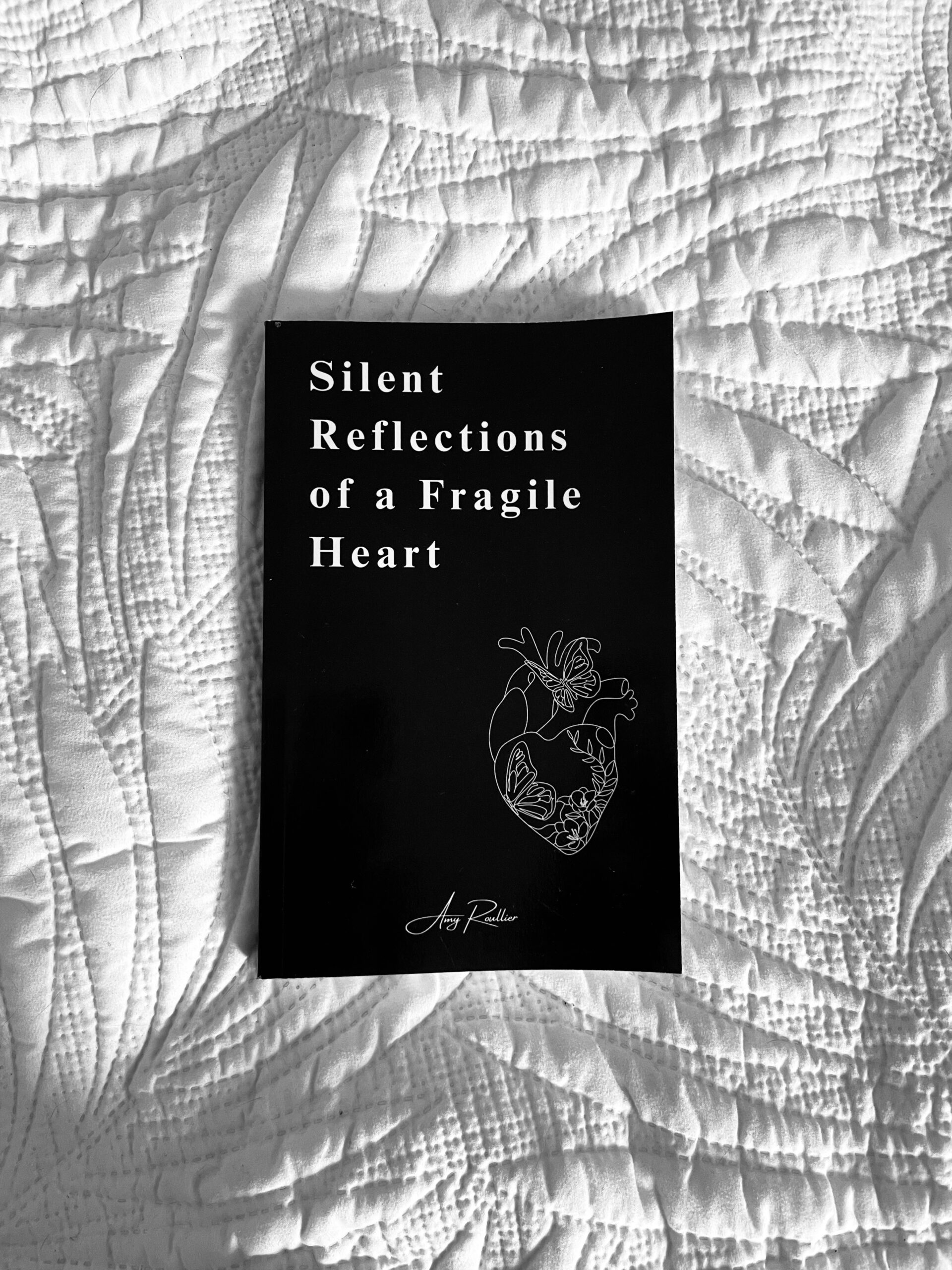 Picture of Amy Roullier's debut poetry book; Silent Reflections of a Fragile Heart, laying on a white duvet